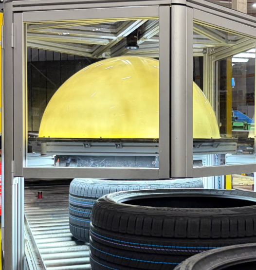 QBIC Tires: Nahansicht der Prüfstation mit gelbem Beleuchtungsdom und Reifen auf dem Förderband